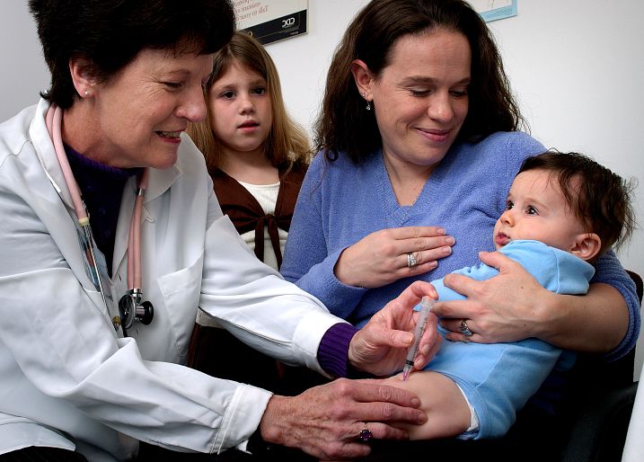 Baby getting a shot with mom and sister