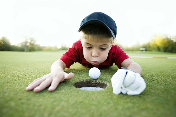 Boy blowing golf ball into the hole